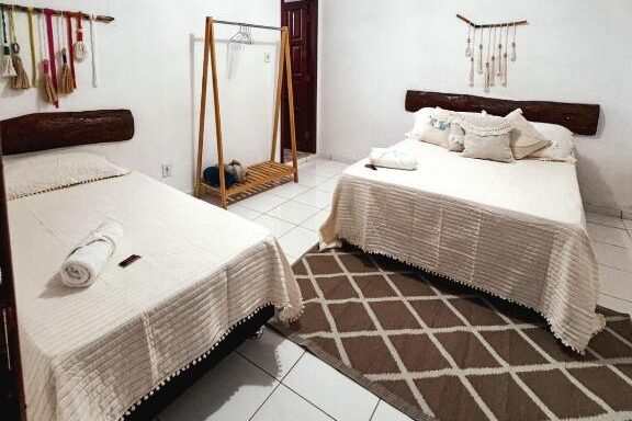 Quarto na Carimbó Pousada e Hostel com cama de casal, mesa de centro e estante de madeira rústica em paredes brancas e teto de madeira.