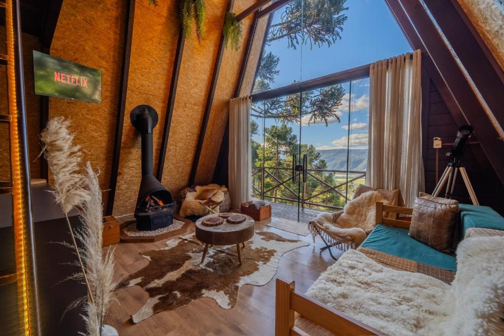 Cabana de madeira moderna com vista panorâmica para a montanha, decorada com tapete de couro, cadeiras forradas e lareira acesa, proporcionando um ambiente acolhedor e relaxante para assistir Netflix, no Chalé Vista do Vale Urubici SC, para representar onde ficar na Serra Catarinense.