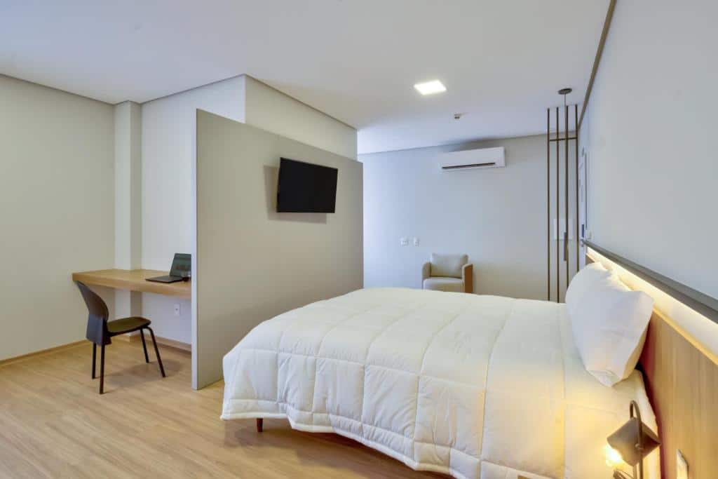 Quarto de hotel Comfort Hotel Serra da Canastra moderno com cama confortável, mesa de trabalho de madeira e televisão de tela plana na parede. Ilustra onde ficar na serra da canastra