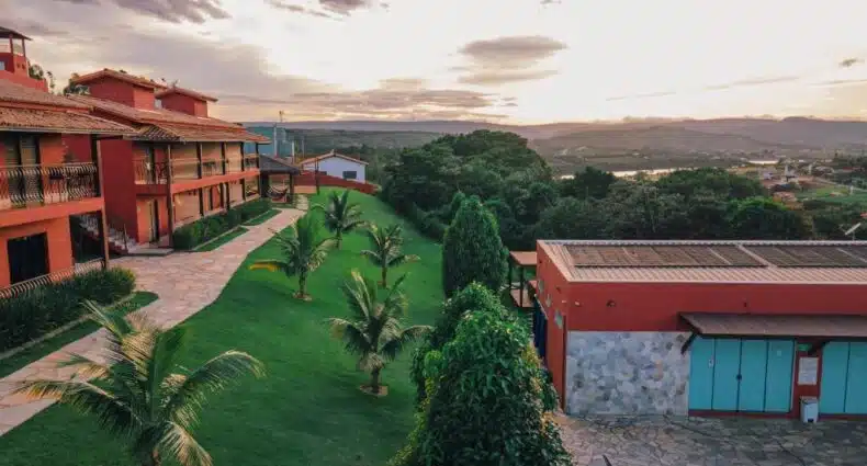 Pôr do sol panorâmico sobre complexo hoteleiro de arquitectura tropical com piscina, gramado e palmeiras em destino turístico brasileiro.