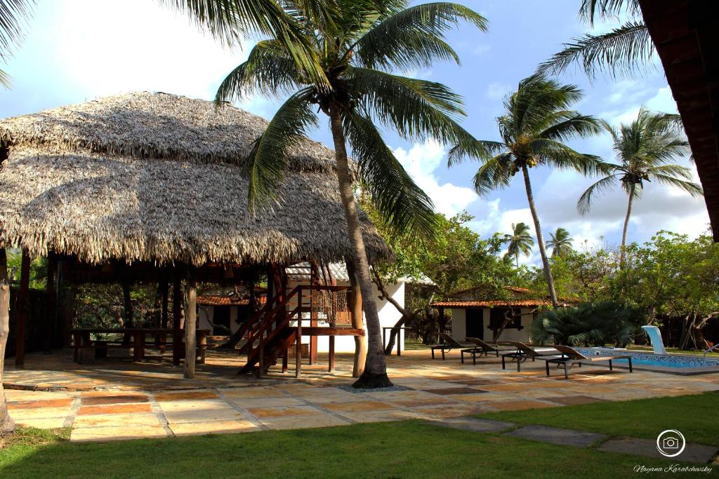 Casa de praia com telhados de palha cercada por coqueiros no Orla Atins com piscina ao fundo em cenário tropical paradisíaco.