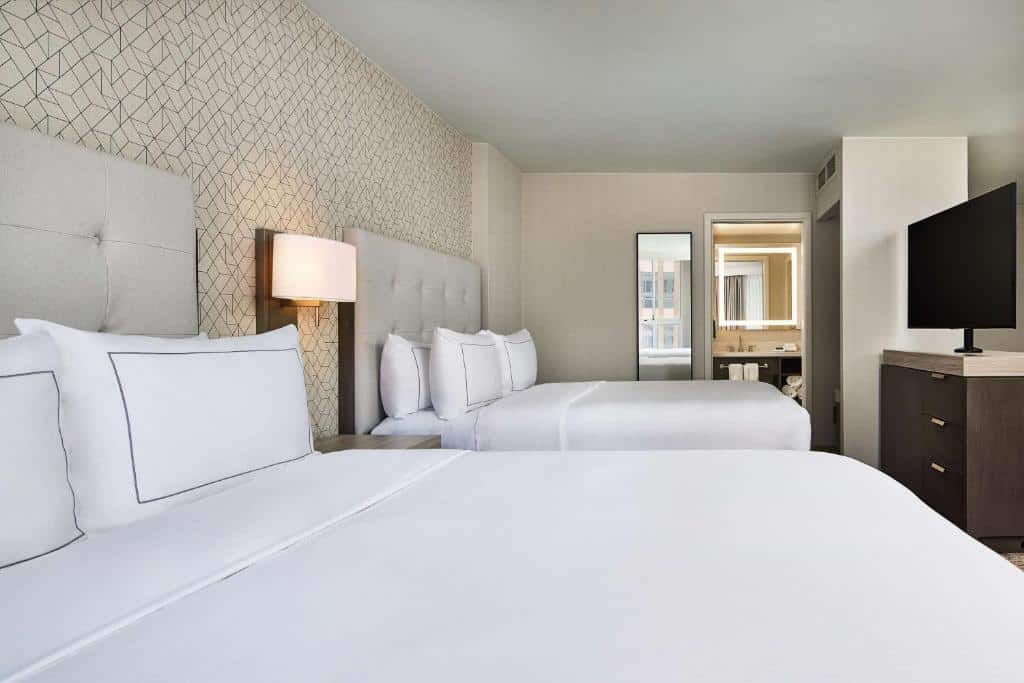 Quarto do Hilton Kansas City Country Club Plaza com paredes geométricas, duas camas de casal brancas, luminária de parede e televisão plana na parede.