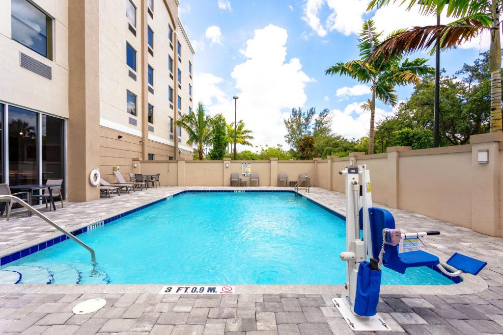 Piscina ao ar livre no Holiday Inn Express & Suites - Miramar by IHG com cadeiras azuis e palmeiras ao fundo