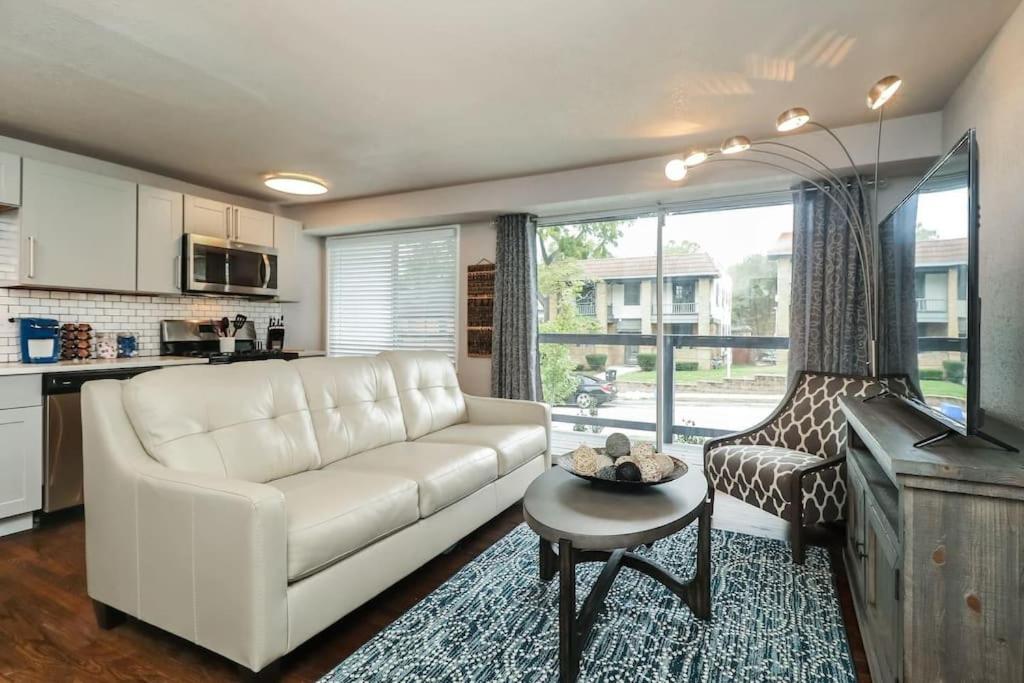 Apartamento mobiliado no Holly Second Floor com sala de estar arejada, sofá de couro bege, mesa de centro de madeira e cadeira estampada próxima a janela com vista externa.