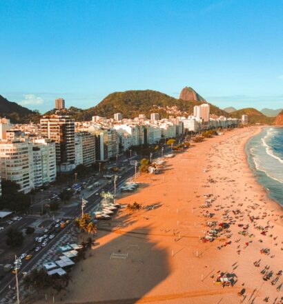 Praia de Copacabana, Rio de Janeiro, com montanhas e edifícios ao fundo, lotada de pessoas na areia em um dia ensolarado, para representar onde ficar em Copacabana.