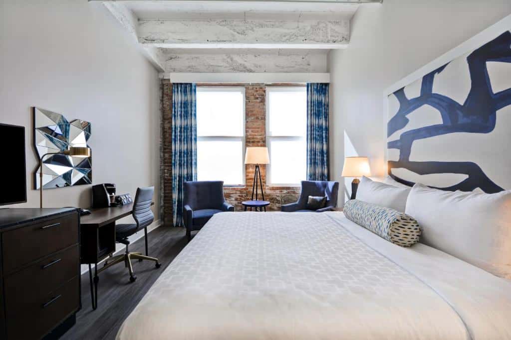 Quarto moderno do Hotel Indigo Kansas City - The Crossroads com decoração em tons de cinza e azul, paredes de tijolos aparentes, sofás e área de trabalho elegantes.