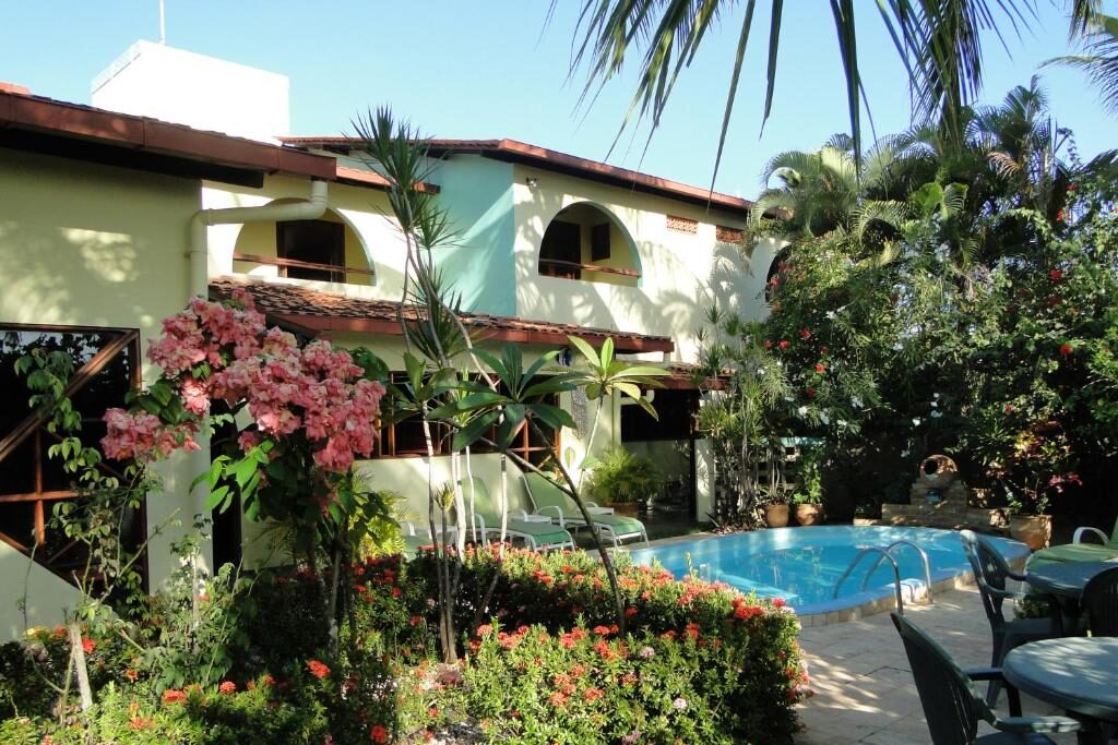 Jardim tropical luxuoso com piscina e palmeiras no Hotel Pousada Arco Íris.