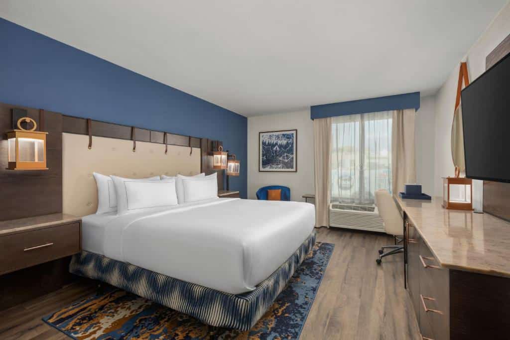 Quarto do Hotel Westport Kansas City com decoração azul e marrom, cama de casal com lençóis brancos, mesa de trabalho e poltrona.