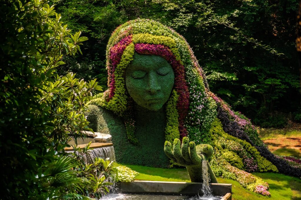 Estátua da Deusa da Terra, uma mulher de corpo inteiro esculpida em flores e folhagens verdes, com expressão serena, no Jardim Botânico de Atlanta.