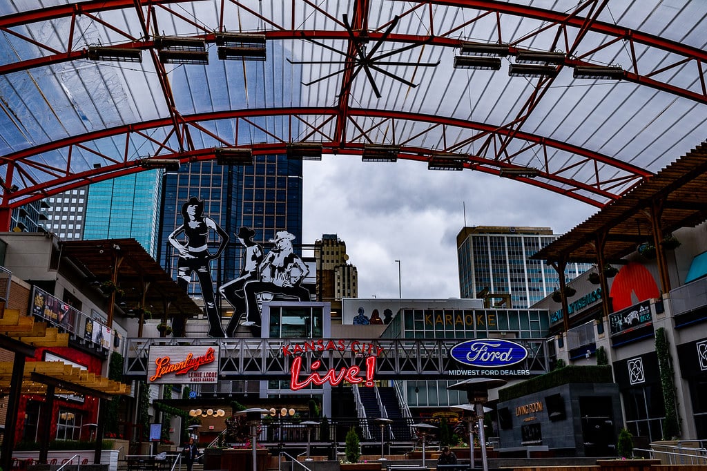 Arquitetura metálica com estrutura vermelha em centro urbano brasileiro, com painéis publicitários, letreiros luminosos e elementos decorativos típicos de distrito comercial e de entretenimento.