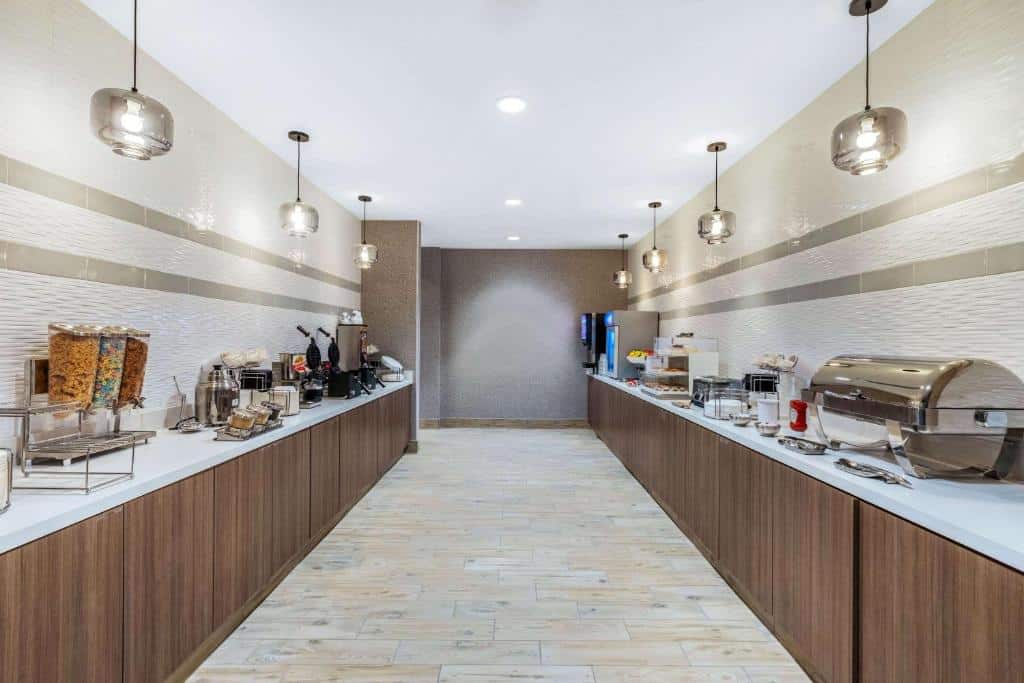 Amplo buffet de café da manhã em restaurante do La Quinta Inn & Suites by Wyndham Kansas City Beacon Hill com balcões de madeira, iluminação suspensa e piso de pedra.