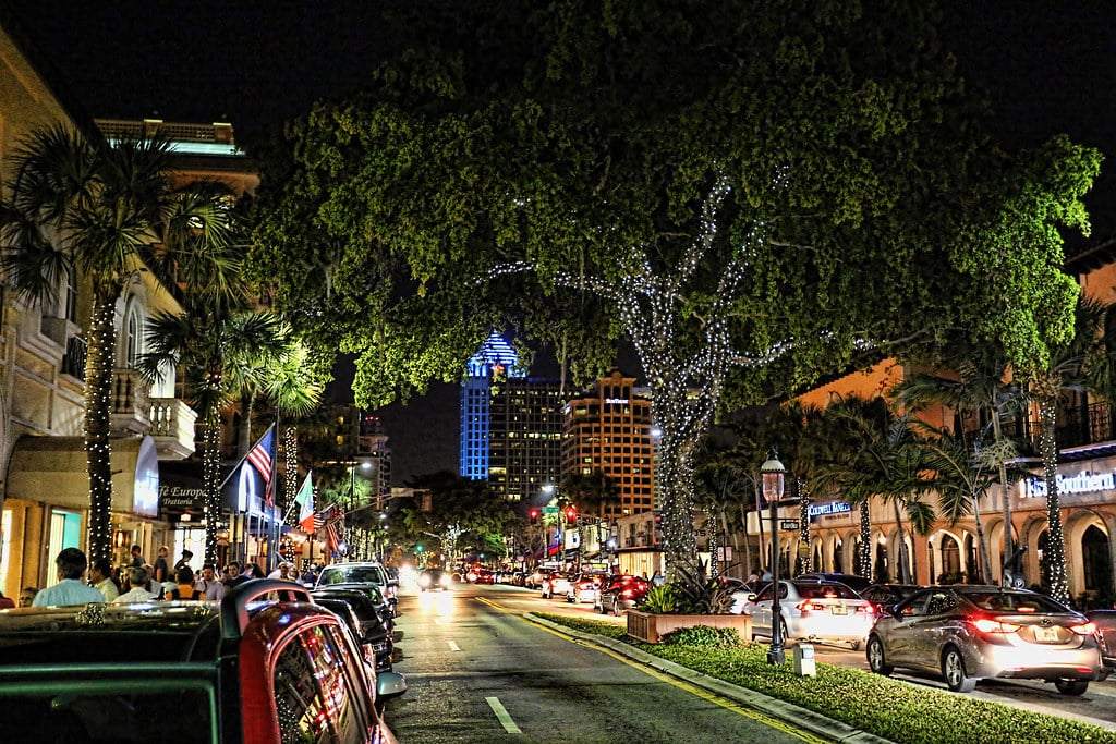 Las Olas Boulevard à noite com edifícios, árvores e carros em movimento no centro da cidade.