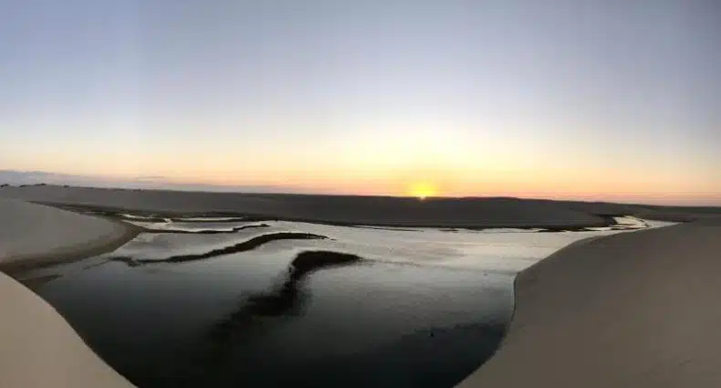 Paisagem de dunas de areia branca dos Lençóis Maranhenses com lagoas e lagos espelhados refletindo o horizonte durante o pôr do sol, foto de divulgação da Maré de Atins Eco Lodge, uma das opções de onde ficar em Atins.