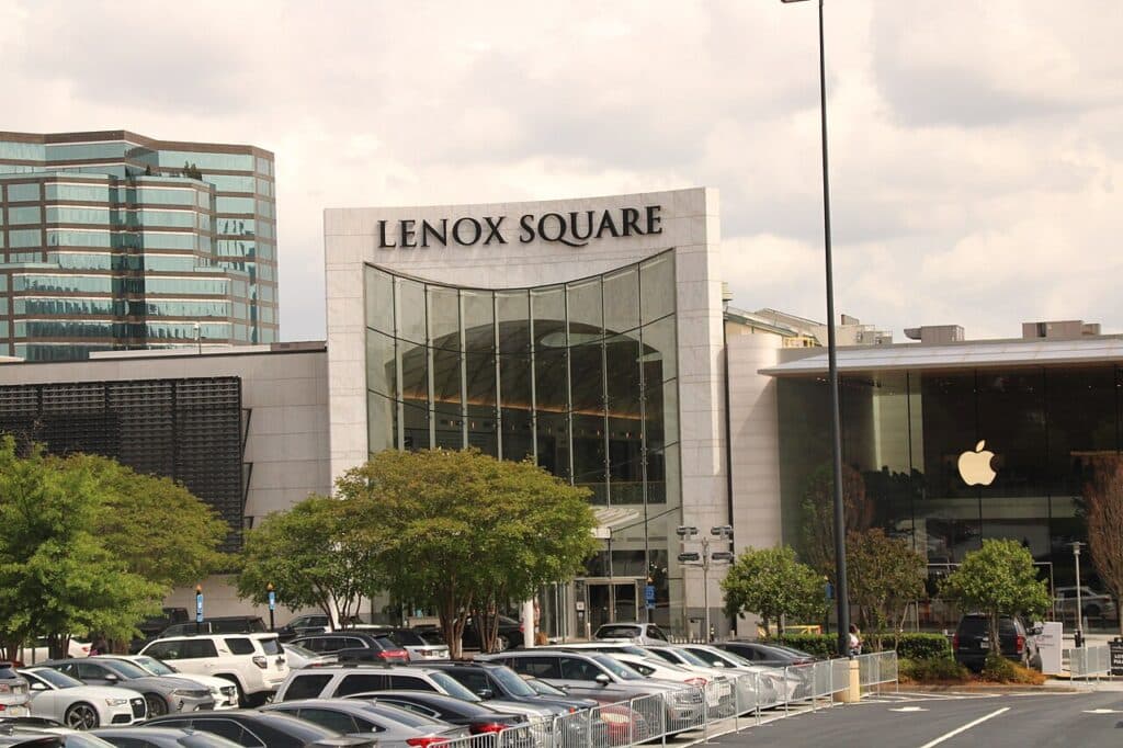 Entrada do Lenox Square, shopping com fachada de vidro e design arquitetônico grande e moderno, situado em meio a árvores e estacionamento em Atlanta.