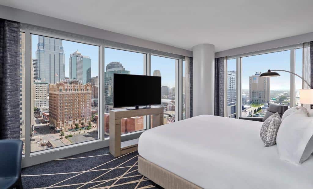 Moderno quarto do Loews Kansas City com vista panorâmica da paisagem urbana de uma grande cidade, incluindo arranha-céus e prédios históricos, refletidos nas janelas de vidro.