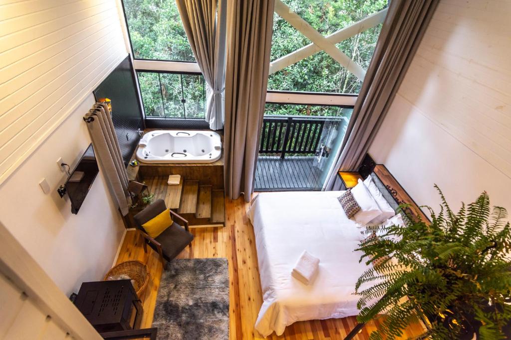Quarto aconchegante de chalé de madeira com janelas amplas, banheira de hidromassagem e vista para a vegetação externa, no Lofts Kayser Haus, para representar onde ficar na Serra Catarinense.