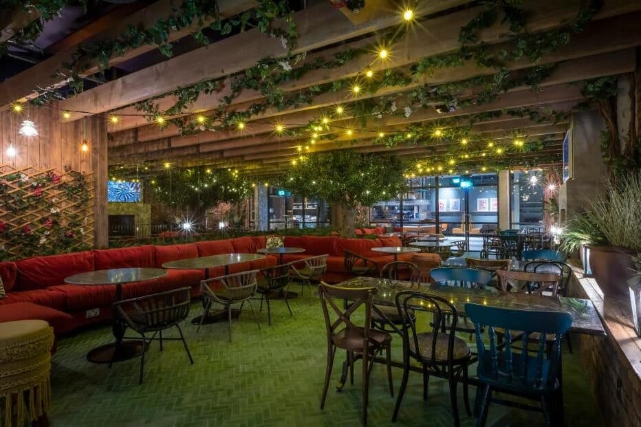 Área externa de restaurante no Marlin Hotel Stephens Green com decoração rústica, cadeiras coloridas e iluminação de luzes penduradas entre treliças de madeira cobertas por plantas.