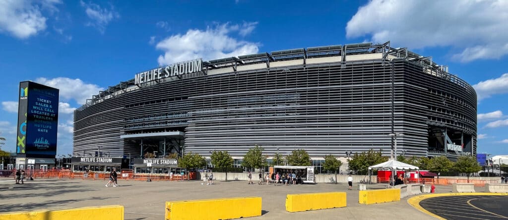 Estádio Metlife, grande arena esportiva moderna em estrutura de concreto preta sob céu azul com nuvens brancas.