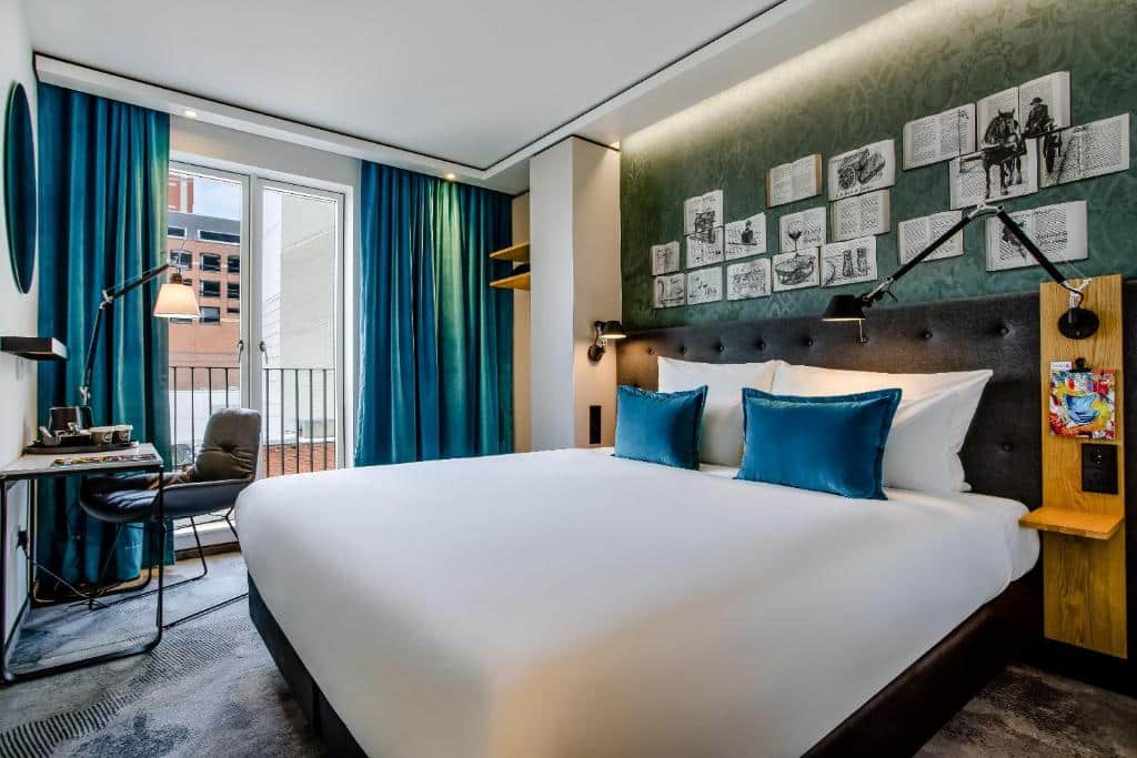 Quarto do Motel One Dublin com paredes verdes, cortinas azuis e decoração em preto e madeira