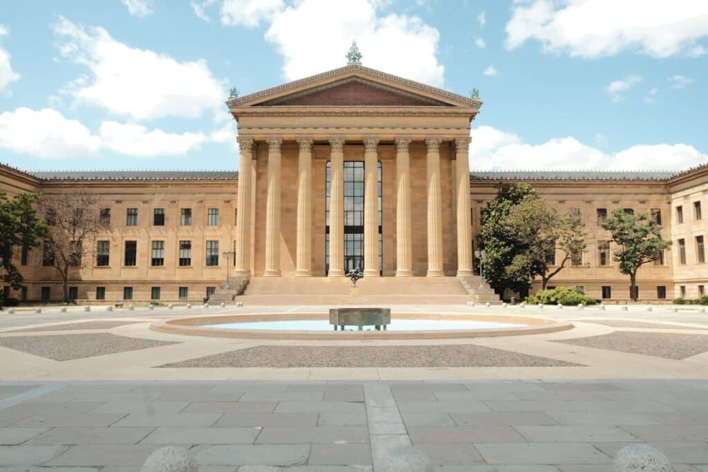 Philadelphia Museum of Art, um prédio de arquitetura clássica com colunas e telhado em estilo grego, refletido em fonte d'água no centro de praça arborizada, para representar o que fazer na Filadélfia.