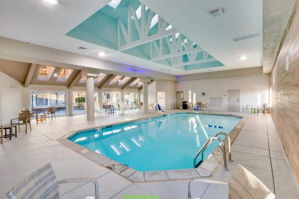 Piscina interna do Orangewood Inn & Suites Kansas City Airport com teto de estrutura metálica em ambiente moderno e aconchegante com móveis confortáveis.