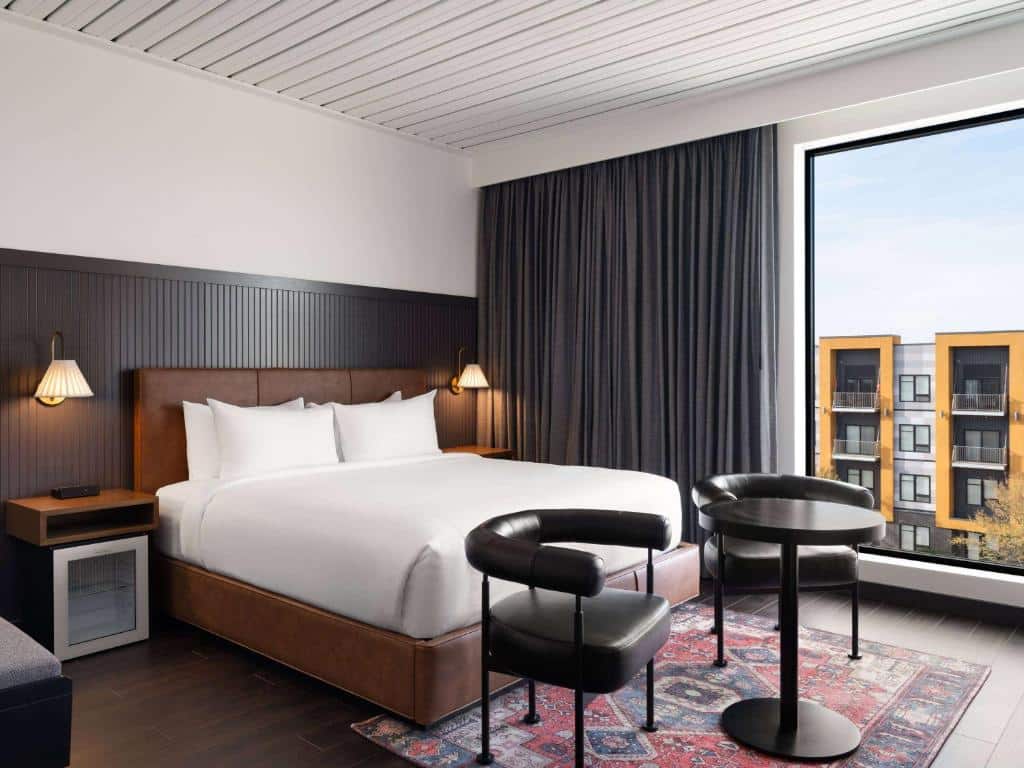 Quarto do Origin Kansas City Riverfront com cama king size, luminária de parede e bela vista da cidade através da janela.