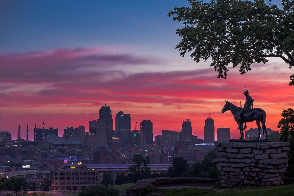 Horizonte urbano da cidade de Kansas City ao pôr do sol com estátua equestre em primeiro plano.