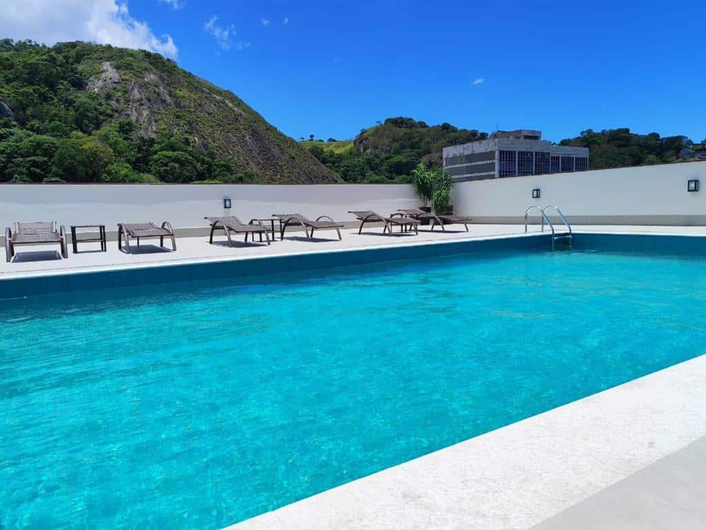 Piscina de azul turquesa do Alice Vitoria Hotel Arte by Nobile cercada por espreguiçadeiras em área de lazer com vista para montanhas verdes e céu azul límpido