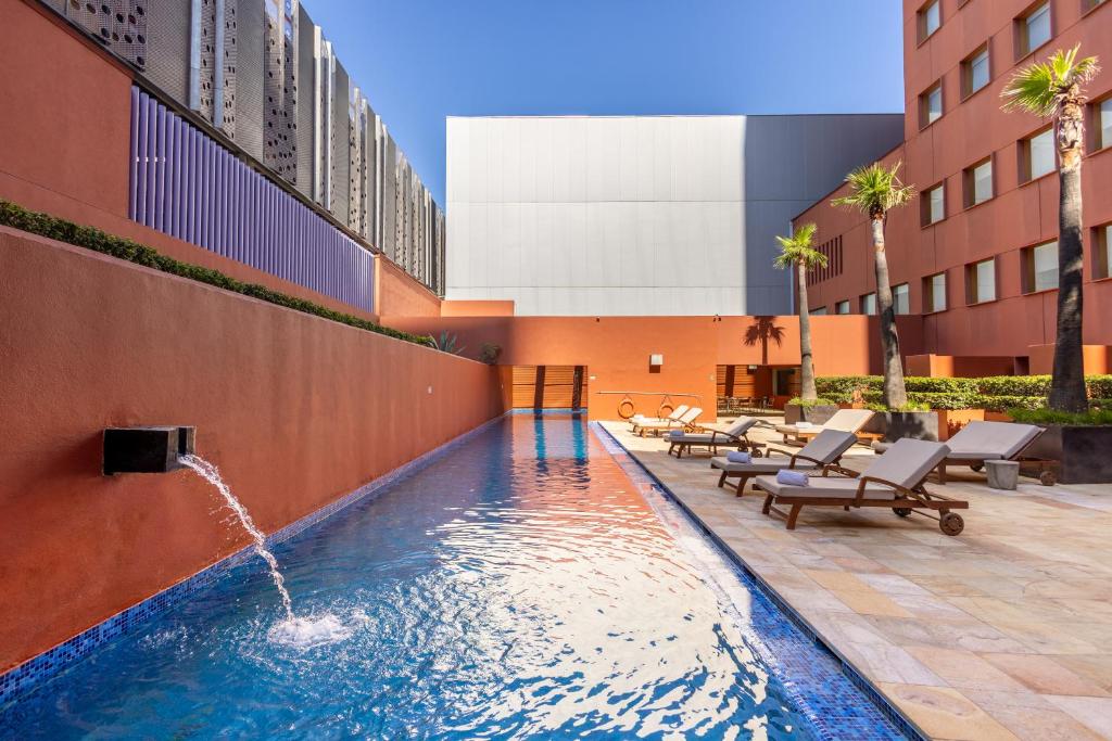 Piscina com deck e espreguiçadeiras em complexo residencial moderno com prédios coloridos ao fundo do Barceló Monterrey Valle. Representa hotéis em Monterrey.