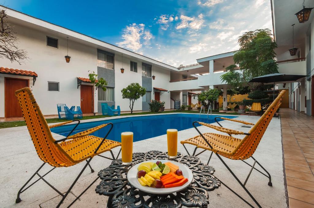 Piscina em área de lazer do Hotel Isabel com cadeiras de veraneio em cores vivas, refrescos e frutas exóticas dispostas em mesa decorada com motivos florais. Representa hotéis em Guadalajara.