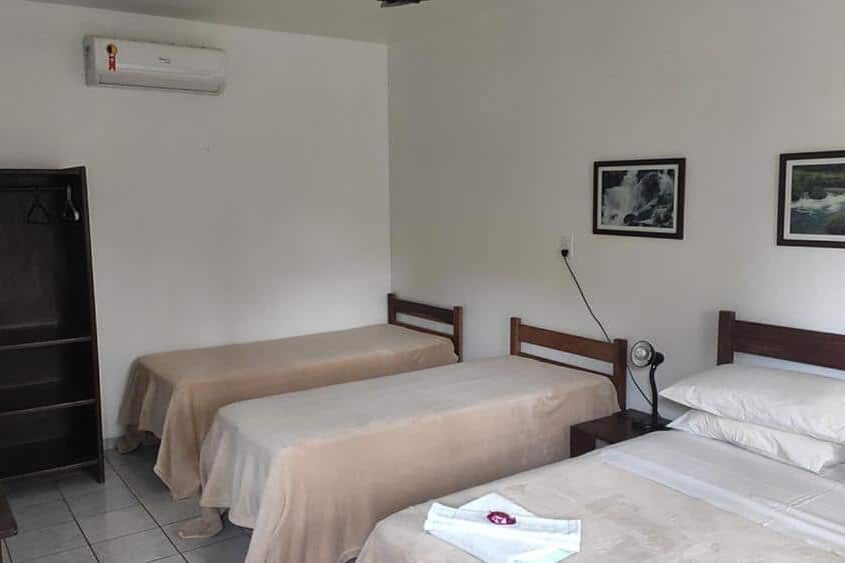 Dois leitos de solteiro em quarto da pousada barcelos com parede branca, armário preto e quadros na parede.