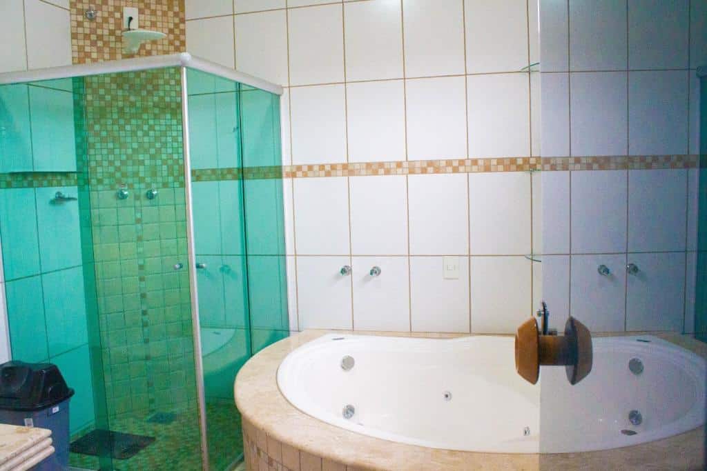 Banheiro de luxo da Pousada Encantos do Glória com paredes decoradas com mosaicos verdes e banheira de hidromassagem circular branca.