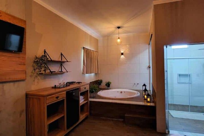 Banheiro rústico e aconchegante com banheira redonda, armário de madeira e espelho na parede na pousada lago azul