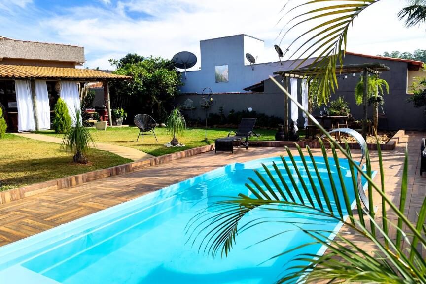 Piscina da Pousada Nascente do São Francisco cercada por plantas tropicais em casa moderna com telhado escuro e móveis de vime na varanda