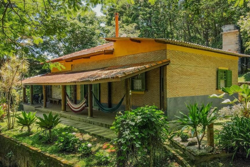 Casa de campo térrea com tijolos amarelos da pousada sitio canto d'água em meio a jardim exuberante na floresta.