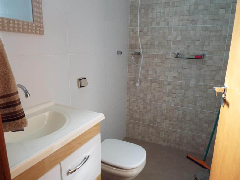 Banheiro com revestimento de azulejos de tons acinzentados, pia com gabinete claro, vaso sanitário e um box de chuveiro com barra de apoio. - pouso glória