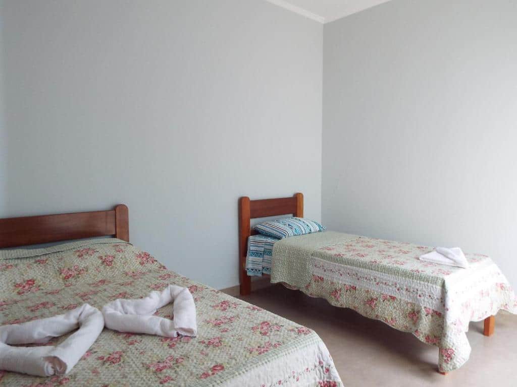 Dois leitos de madeira com colchas florais e listradas em quarto ensolarado e de paredes claras. - pouso glória