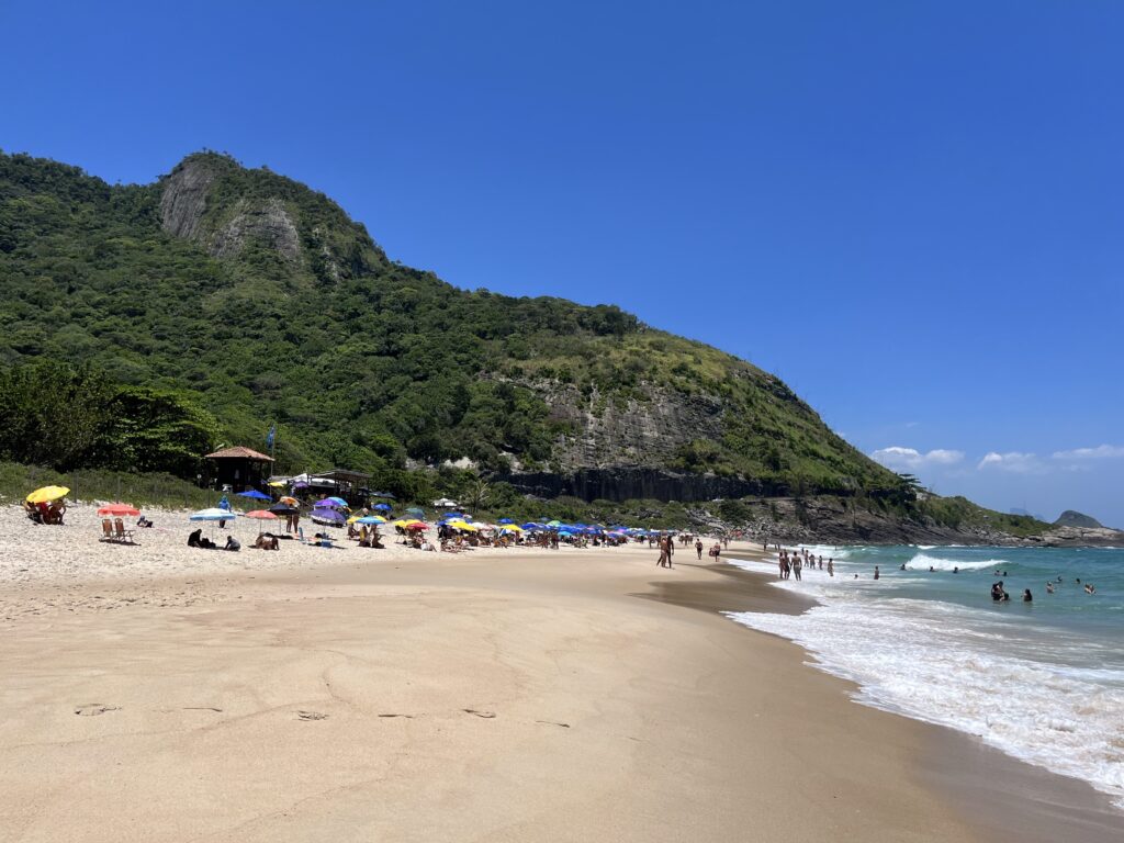 Praia de areia com guarda-sóis coloridos e montanhas verdes ao fundo em dia ensolarado no Rio de Janeiro