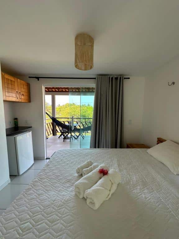 Quarto aconchegante do Atins Suites, uma das opções de onde ficar em Atins, com varanda, cama casal com roupa de cama clara, frigobar e luminária de bambu pendente.