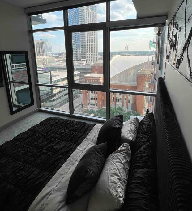 Quarto do Opulence is a way of life com vista panorâmica da cidade, cama com travesseiros pretos e cinza, tapete marrom escuro, parede com arte abstrata, janelas amplas com vista para edifícios e ruas da cidade, sendo uma opção de onde ifcar em Dallas.