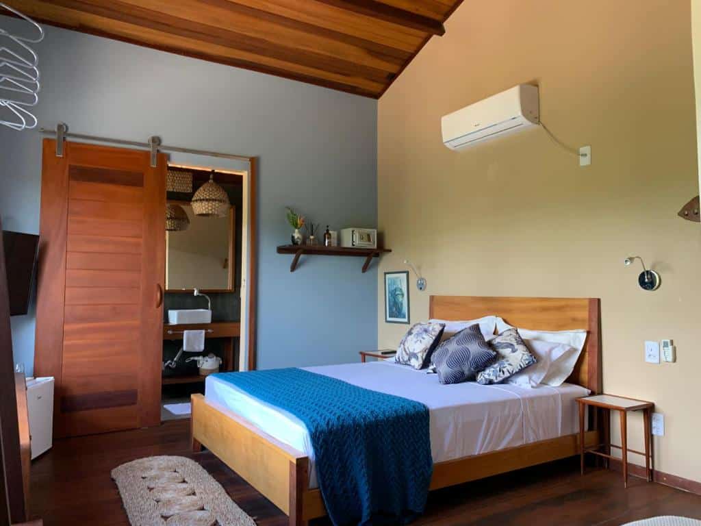 Quarto do Vila das Águas, uma das opções de onde ficar em Atins, com cama de casal, prateleira de madeira na parede, ar-condicionado e decoração rústica e natural.