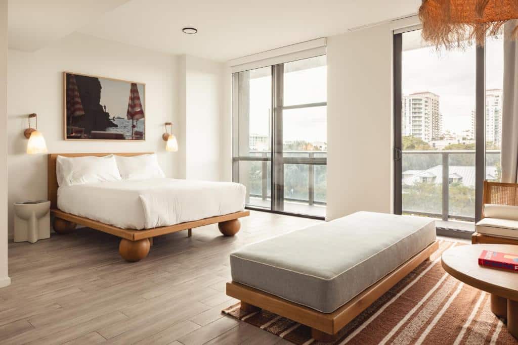 Quarto do Flow Fort Lauderdale Hotel com ampla janela com vista para a cidade, cama king size com lençóis brancos, mesa de cabeceira de madeira e luminária de teto com design exclusivo.