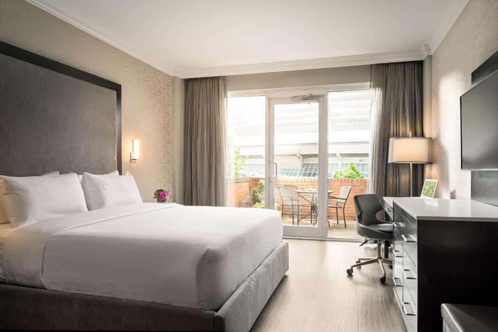 Quarto do Georgian Court Hotel com cama king size, cortinas escuras, móveis e poltrona de escritório, e vista para varanda com mesa e cadeiras.