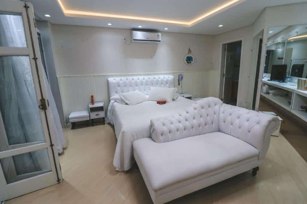 Quarto aconchegante no Paraíso do Salto com cama de casal estofada branca, poltrona combinando e móveis modernos em tons neutros, para representar onde ficar na Serra Catarinense.