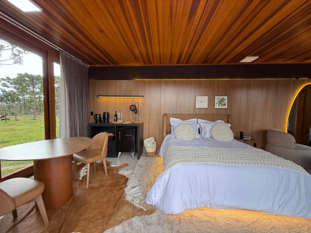 Quarto aconchegante em chalé de madeira com teto de madeira, móveis de couro bege e detalhes decorativos rústicos em meio à natureza, na Pousada Maçã Araucária, para representar onde ficar na Serra Catarinense.