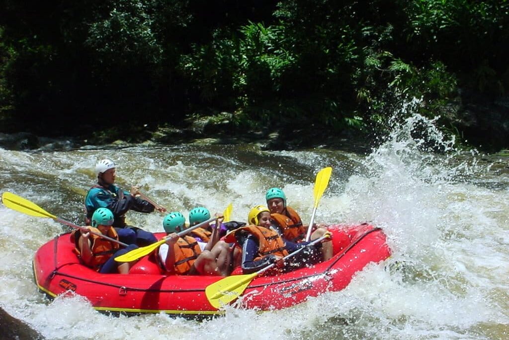 Grupo de pessoas em jangada vermelha navegando por rio caudaloso na natureza exuberante de são luiz do paraitinga.