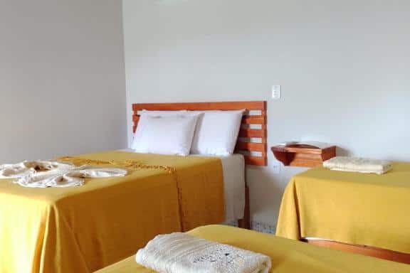 Quarto com cama de casal do Refúgio Pé da Serra – Chalés, roupa de cama amarela, decoração rústica com teto de madeira e ar-condicionado na parede.