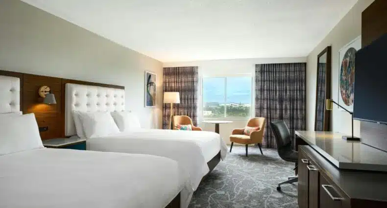 Quarto moderno do Renaissance Meadowlands Hotel e espaçoso com camas de casal, poltronas confortáveis e vista panorâmica da cidade através da janela. Imagem para ilustrar post sobre onde ficar perto do MetLife Stadium.