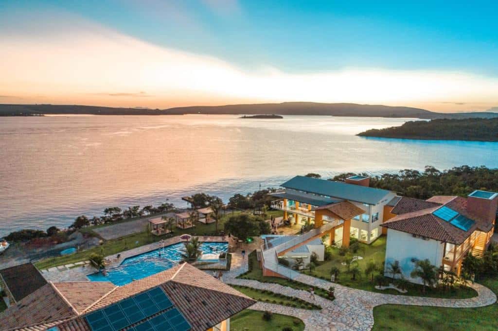 Vista aérea do Riviera Capitólio Hotel de luxo com piscinas e construções em meio à natureza à beira de bela lagoa durante o pôr do sol. Ilustra onde ficar na serra da canastra