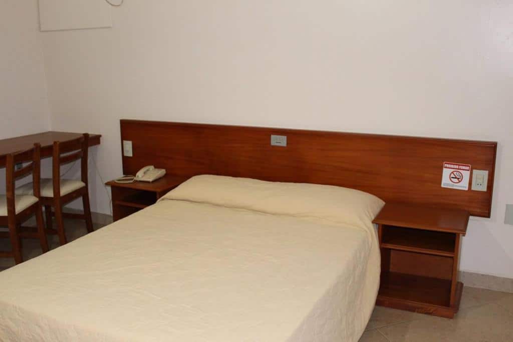 Quarto de hotel (Sacramento Palace) com cama de casal, mesa de cabeceira de madeira e cadeira.